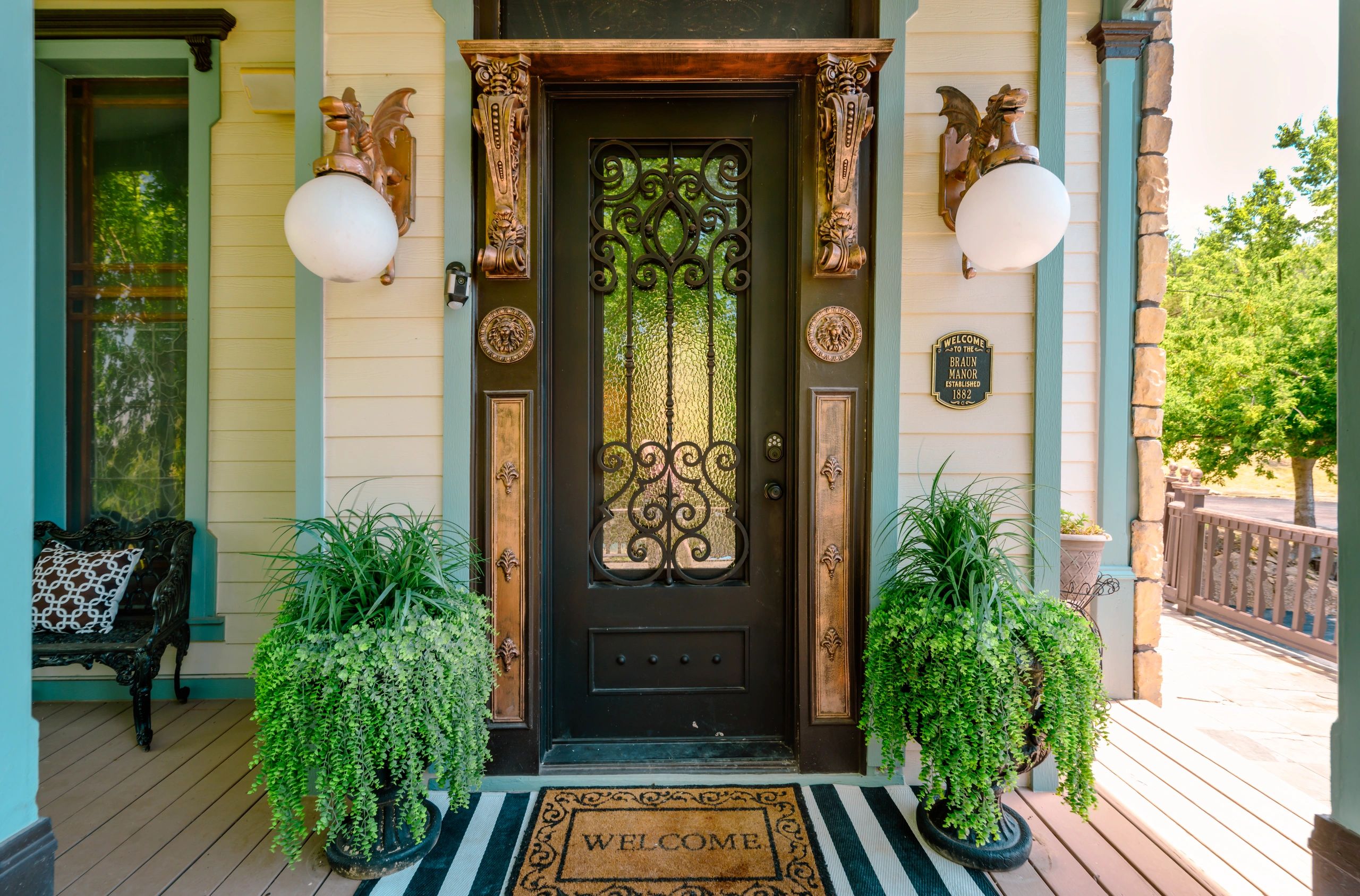 Ornate black door with dragon lamps and welcoming plants on a porch.