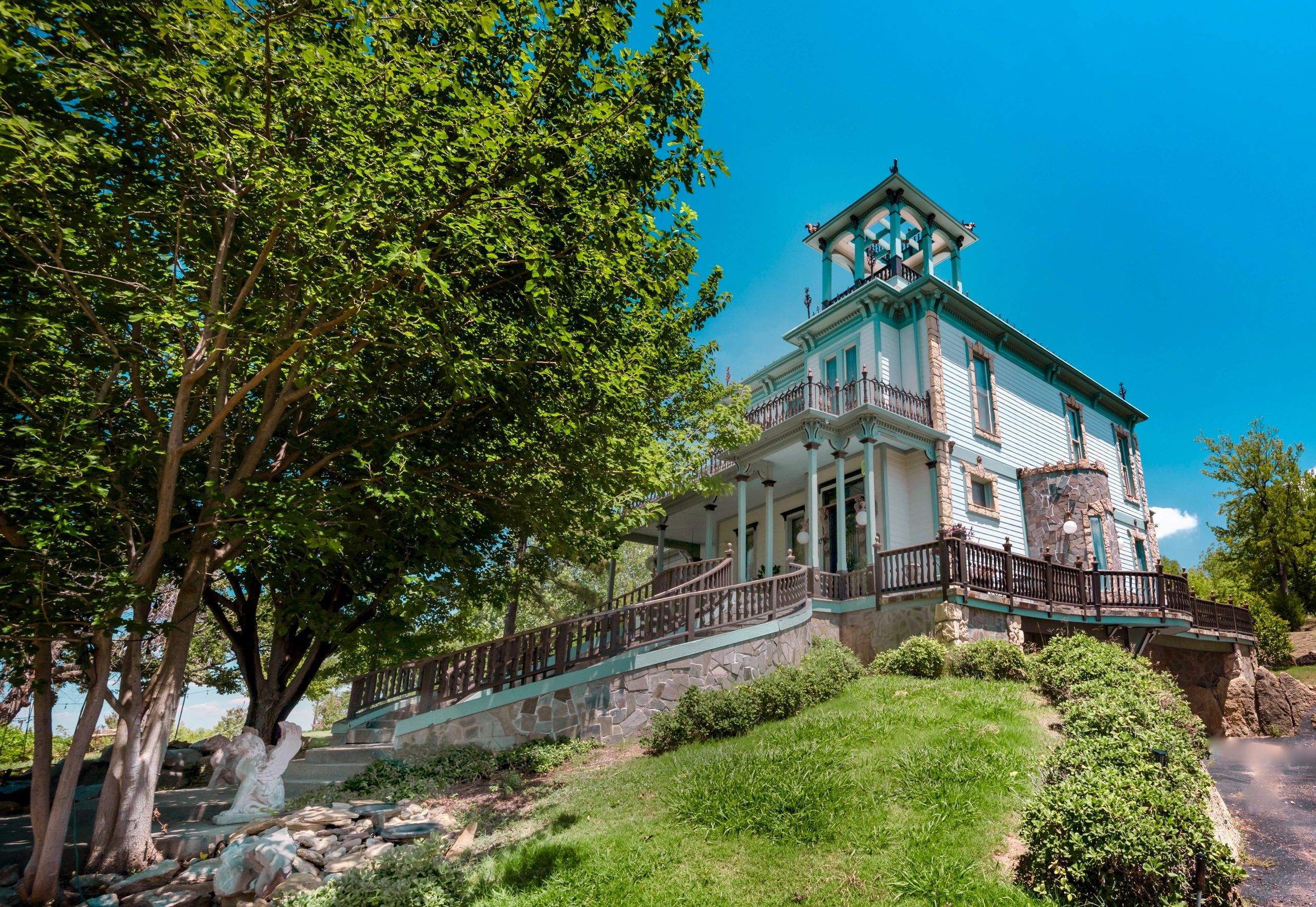 Victorian-style house on a hill with lush greenery and clear blue sky.