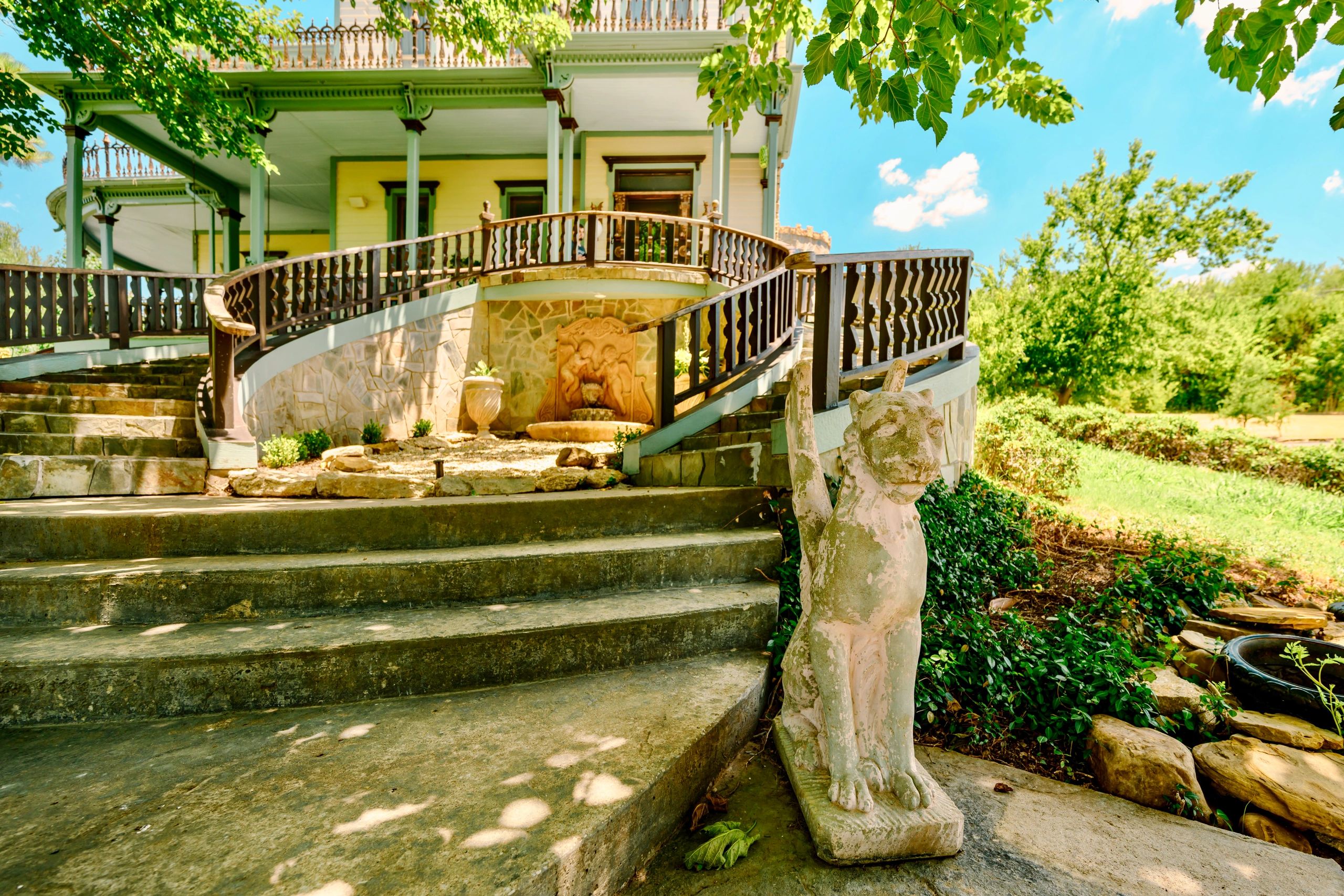 Stone steps leading to a porch with a dog statue and lush greenery.
