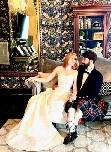 Bride and groom in elegant attire sitting on a vintage sofa.