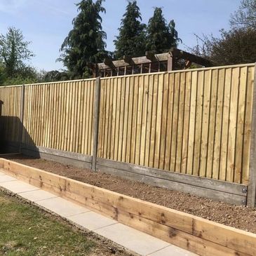 Closeboard wooden fence with wooden sleepers as a retaining wall for the flower bed. 