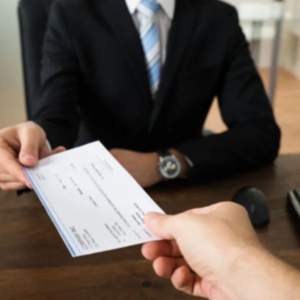 A businessperson is receiving a payroll check from an office worker.