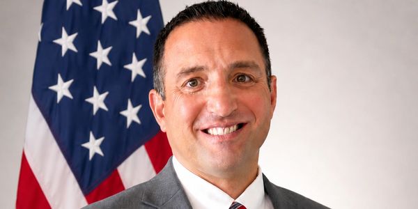 Man in suit smiling in front of American flag.