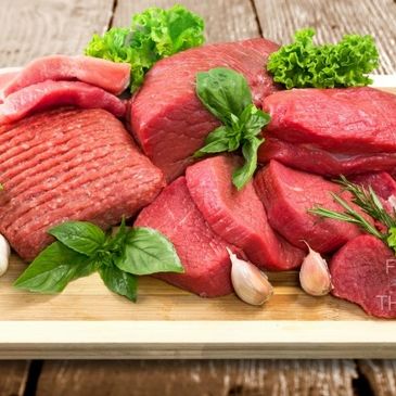 Assorted fresh raw beef cuts garnished with herbs on a wooden board.