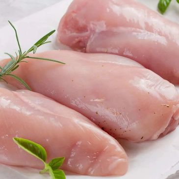 Raw chicken breasts with herbs on a white surface.