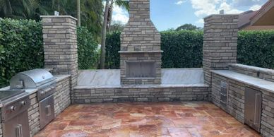 A U-shaped outdoor kitchen and tall fireplace, seating, and matching custom columns for cover.