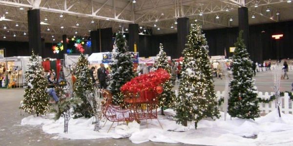 Indoor Christmas display with decorated trees and a sleigh amid artificial snow.
