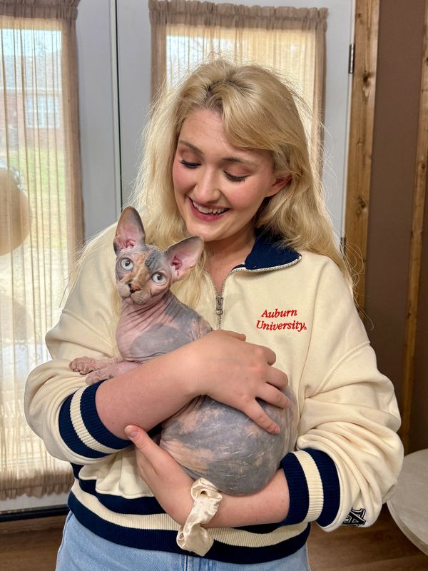 A smiling woman in an Auburn University sweater holds a hairless Sphynx cat.