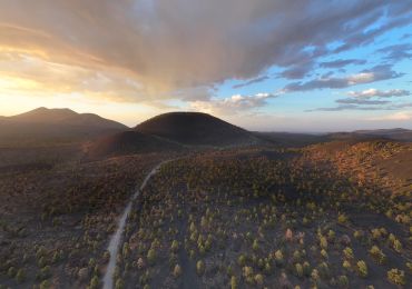 Sunset over volcanic hills with scattered trees and dramatic clouds.
