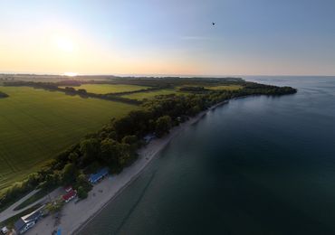 Sunset over a serene coastal landscape with green fields and a calm lake.