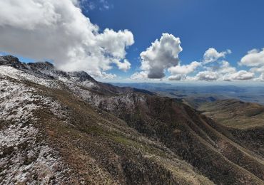 Snow-dusted mountains under a bright blue sky with fluffy clouds.
