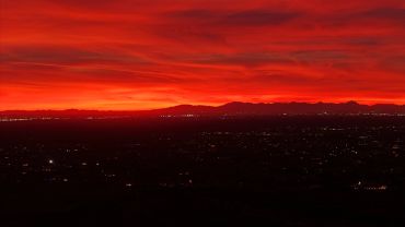 Vibrant red sunset over city and mountain range.
