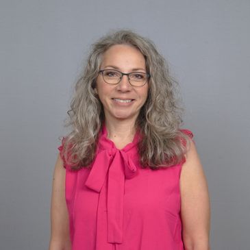 Smiling woman with glasses in a bright pink sleeveless blouse.