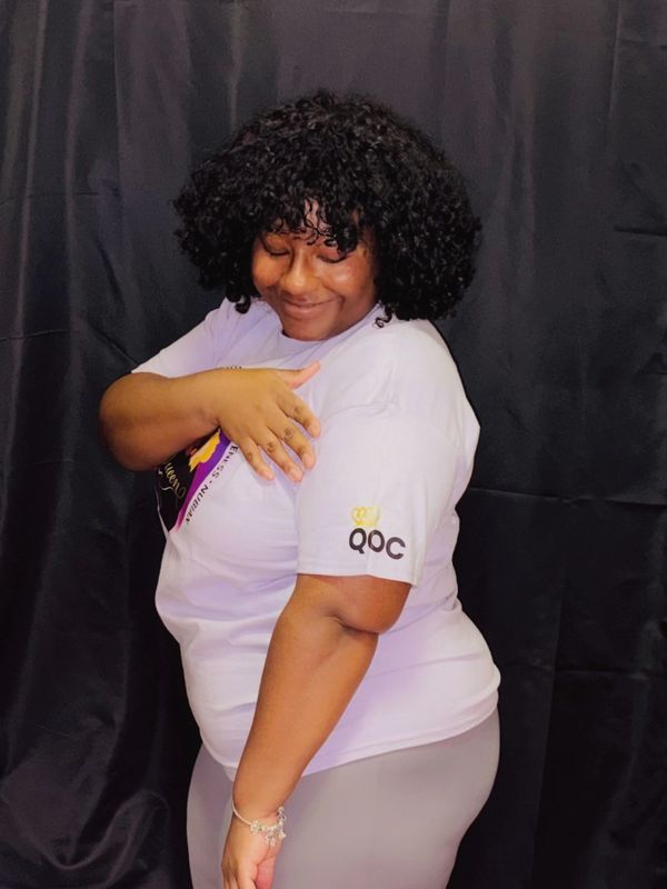 Smiling woman with curly hair in white t-shirt posing sideways.