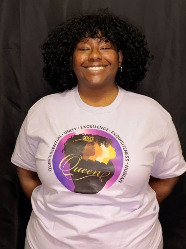 Smiling woman wearing a shirt with 'Queen' graphic and empowering words.