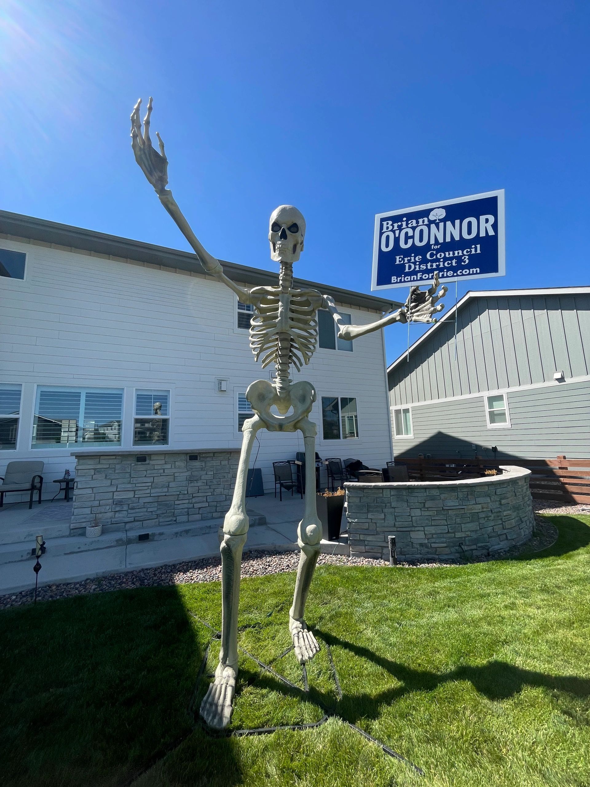 Skeleton holding a political campaign sign in a yard.