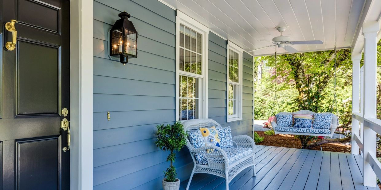 Cozy blue porch with white wicker furniture and a swing overlooking greenery.