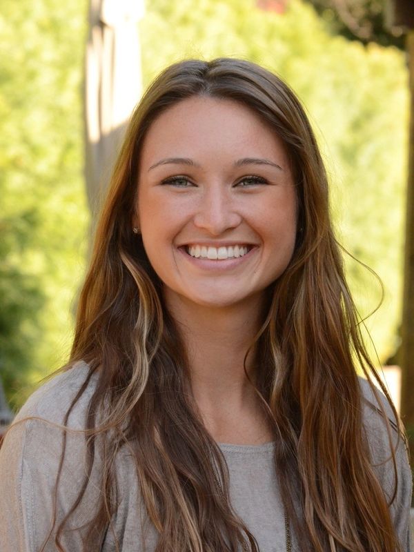 Young woman with long hair smiling outdoors in natural light.