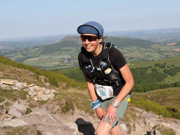 Jen Benson power hiking uphill on a warm sunny day in an ultra race with a big smile
