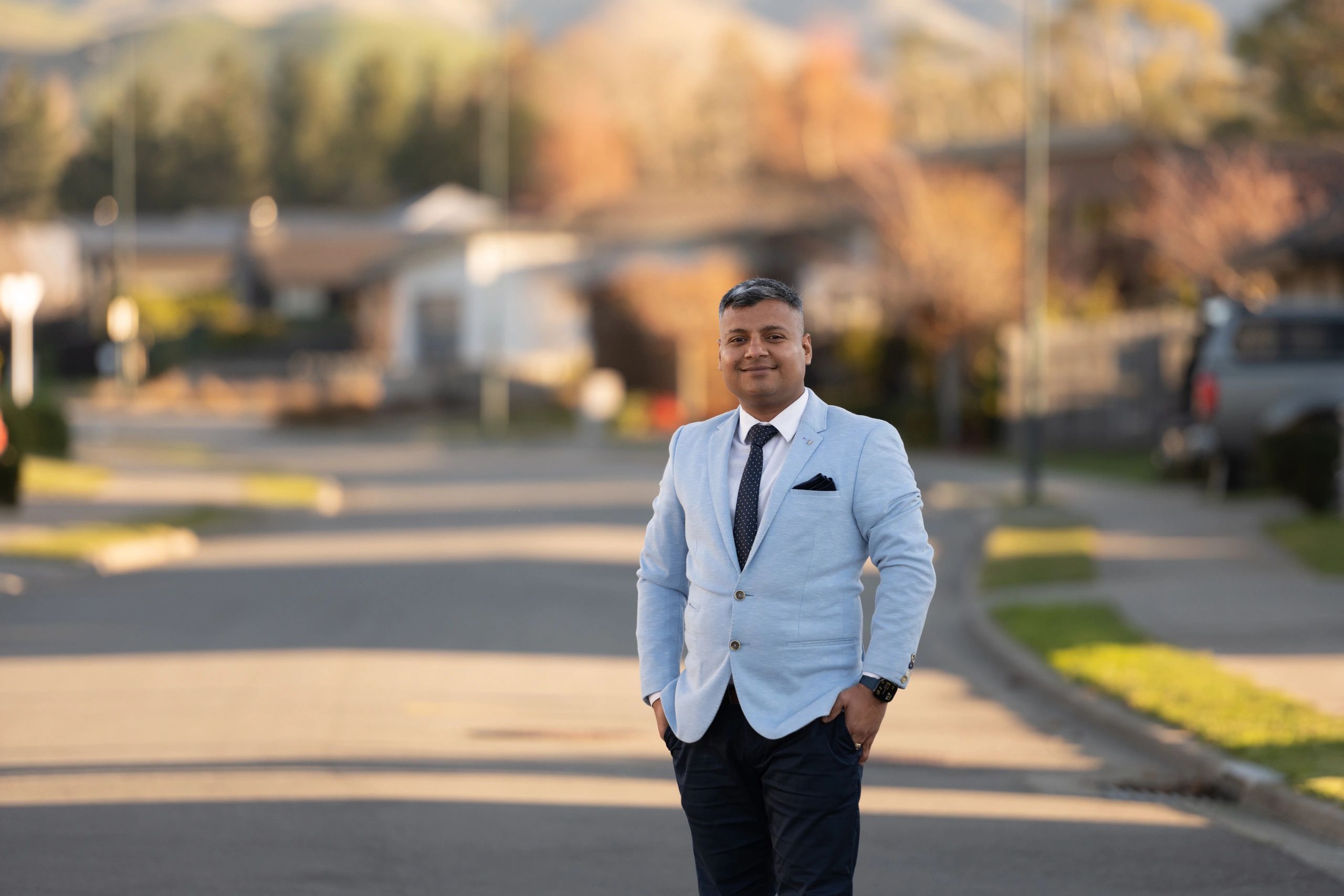 Man in light blue blazer posing outdoors.
