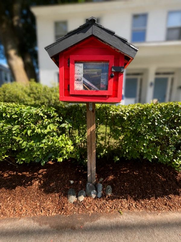 Red little library box on wooden post.