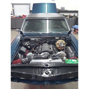 Car with open hood revealing engine bay in garage.