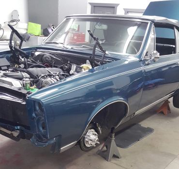 Classic blue car undergoing restoration on jack stands.