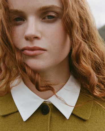 Close-up portrait of a woman with red curly hair and green jacket.