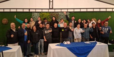 A large group of people posing happily indoors with raised hands.
