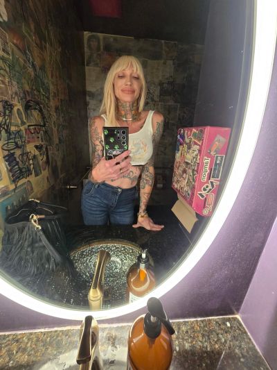 Woman taking a mirror selfie in a tattooed, casual look.