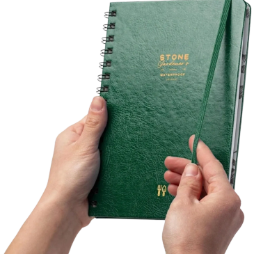 Hands holding a green spiral notebook with elastic band.
