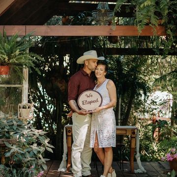 Couple holding a 'We Eloped' sign in a garden setting.