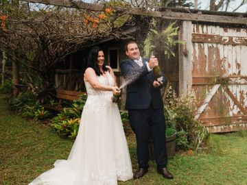 Bride and groom celebrating by popping champagne outdoors.