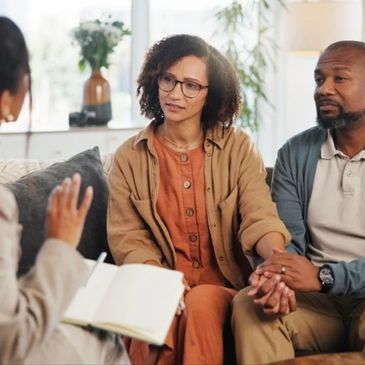 Couple holds hands while attentively listening to a therapist in a counseling session.