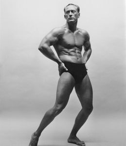 Black and white photo of a muscular man in black briefs.