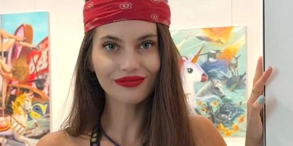 Young woman with red bandana and bright red lipstick smiling indoors.