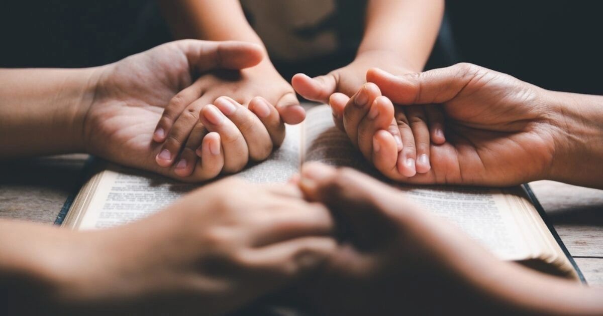 Hands joined in prayer over an open book, symbolizing unity and faith.