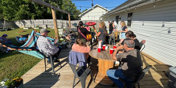 Group enjoying music and drinks on a sunny backyard deck.