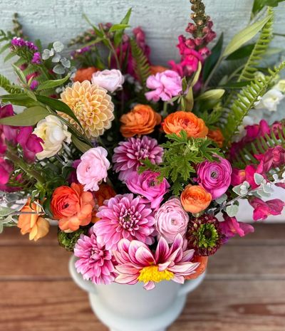 Vibrant mixed flower bouquet with pink, orange, and peach blooms in a white vase.