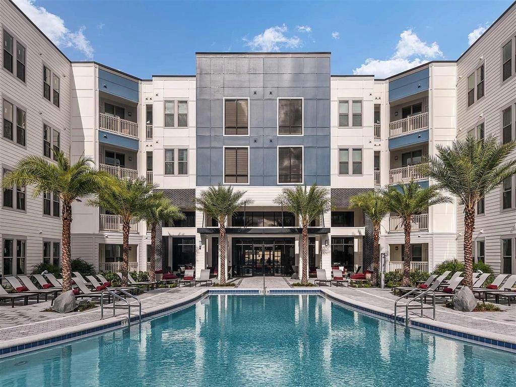 Modern apartment complex with a central swimming pool and palm trees.