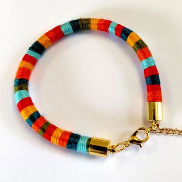A vibrant  coloured handmade thread wrapped bracelet with a gold coloured clasp. Available online.