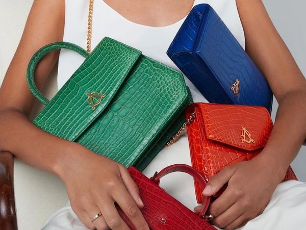 Person holding four vibrant croc-embossed handbags in green, blue, red, and orange.