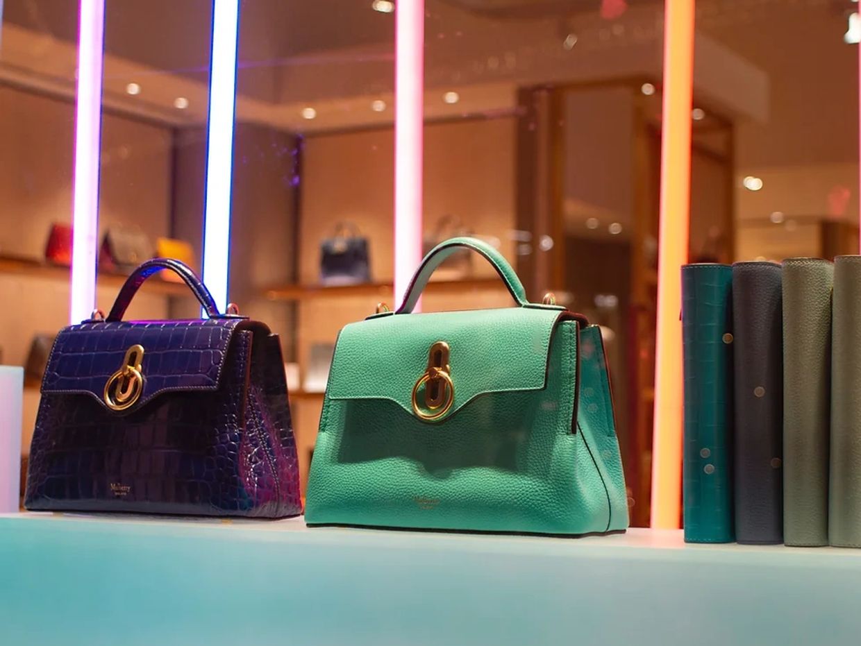Two stylish handbags displayed with colorful vertical lights in the background.