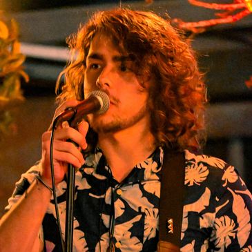 Young man with curly hair singing into a microphone.