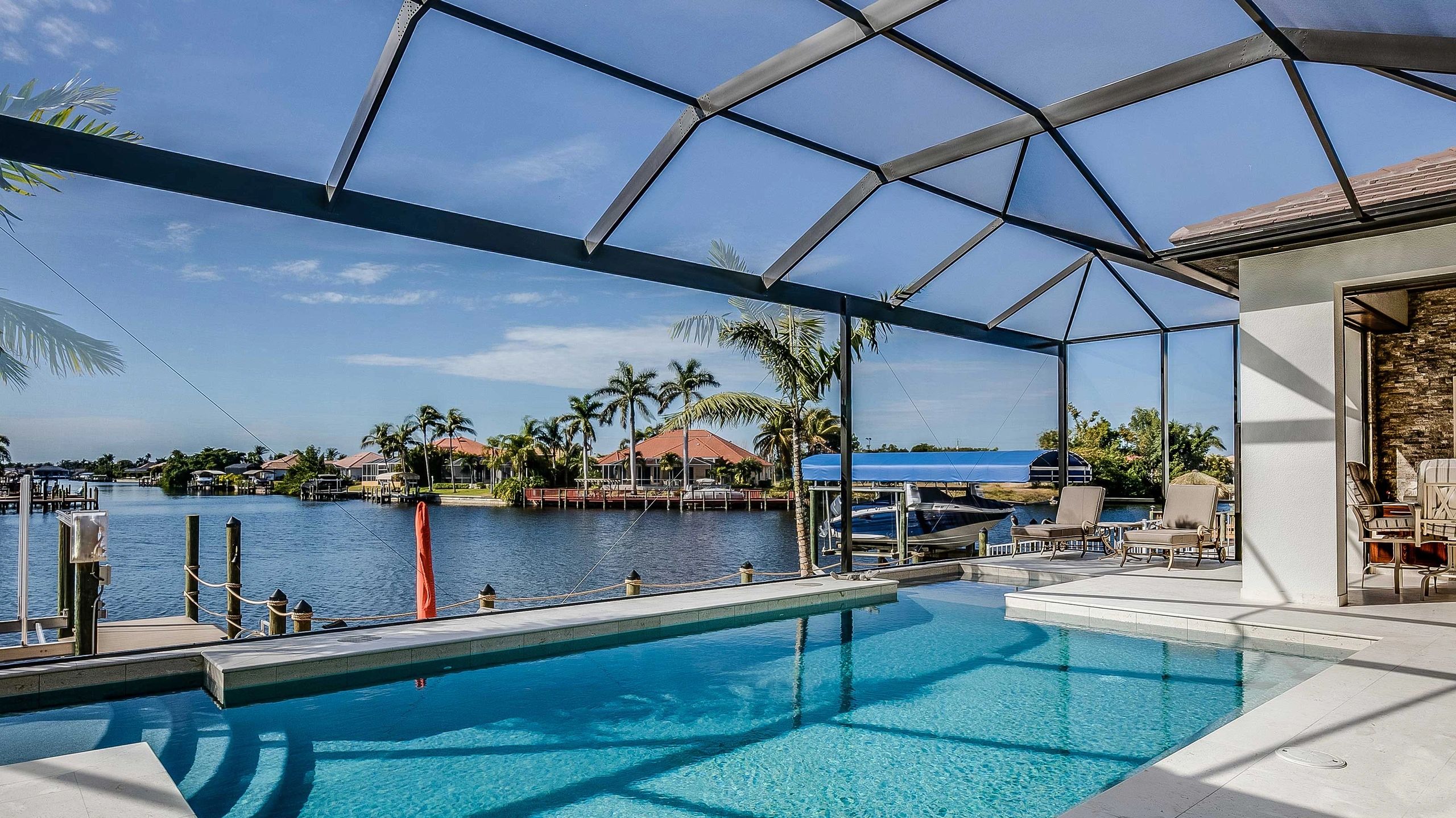 A serene poolside with clear water overlooking a canal and palm trees.