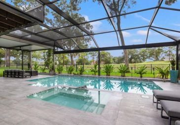 Modern screened-in patio with pool and spa overlooking a green landscape.