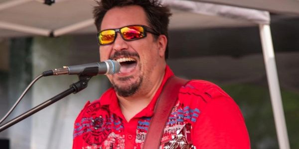 Man singing into microphone with red shirt and sunglasses.