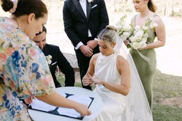 Bride signing marriage documents at outdoor wedding ceremony.