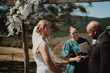 Bride and groom smiling during an outdoor wedding ceremony with officiant.