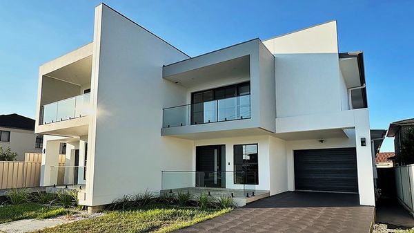 Modern two-story white house with glass balconies and a black garage door.